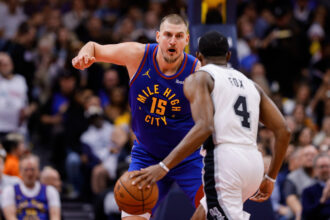 Nov 28, 2025; Denver, Colorado, USA; San Antonio Spurs guard De'Aaron Fox (4) controls the ball as Denver Nuggets center Nikola Jokic (15) guards in the second quarter at Ball Arena. Mandatory Credit: Isaiah J. Downing-Imagn Images