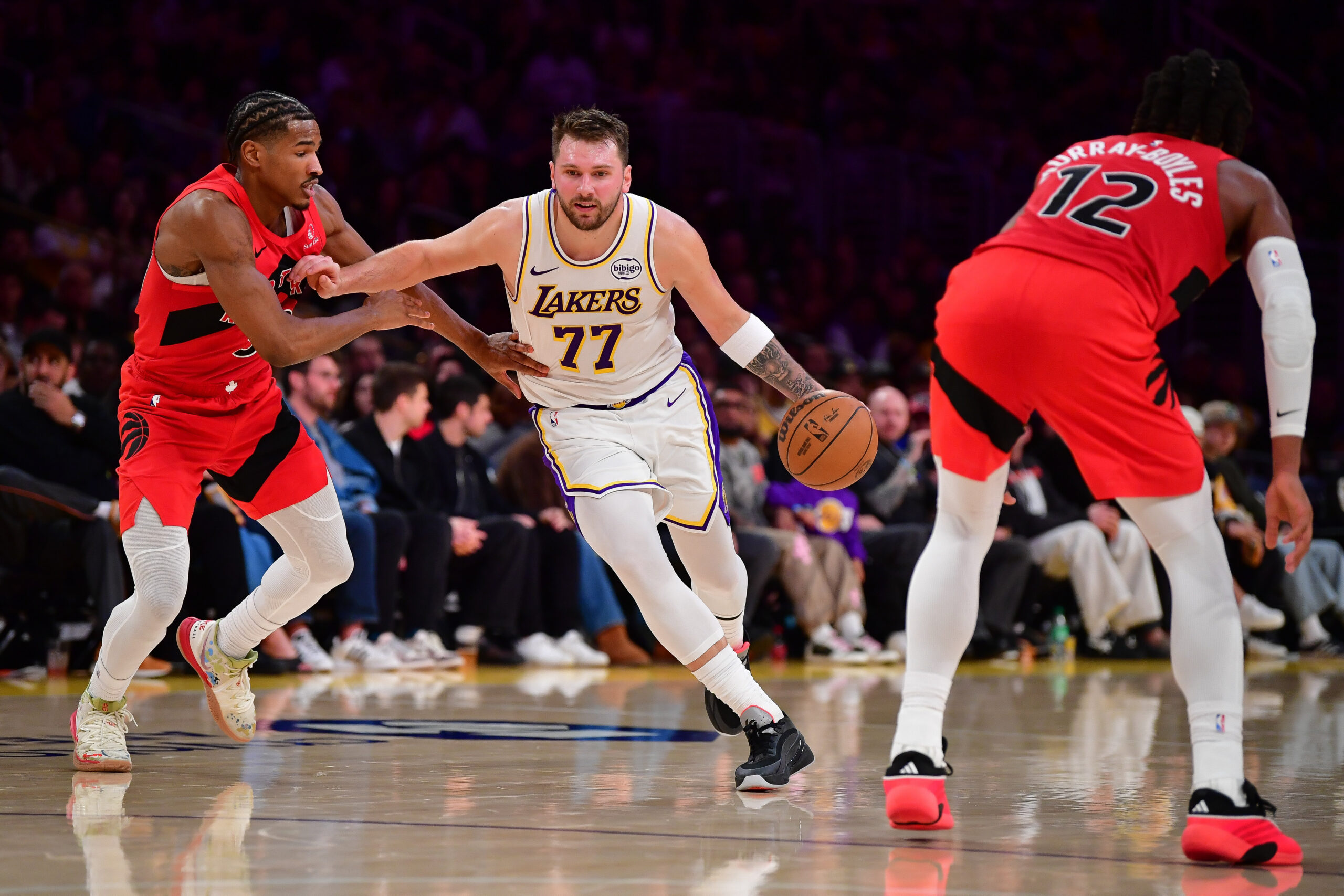 Jan 18, 2026; Los Angeles, California, USA; Los Angeles Lakers guard Luka Doncic (77) moves the ball against Toronto Raptors guard Ochai Agbaji (30) and forward Collin Murray-Boyles (12) during the first half at Crypto.com Arena. Mandatory Credit: Gary A. Vasquez-Imagn Images